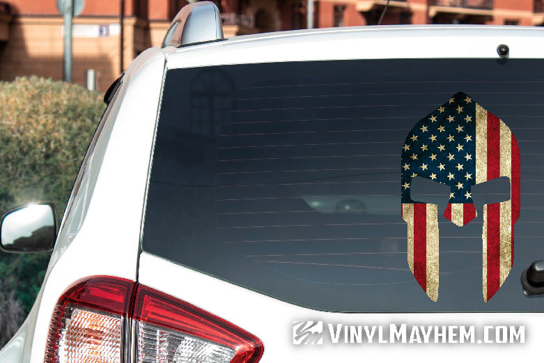 Car with a Spartan helmet decal featuring the American flag on the back window, with 'Vinyl Mayhem' branding.